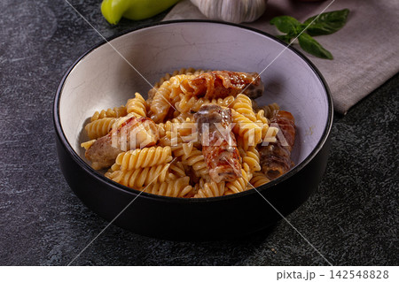 Fusilli pasta with bacon wrapped sausages in creamy sauce served in black bowl 142548828