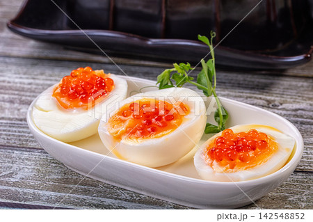 Boiled egg halves topped with red caviar on white plate with green garnish 142548852