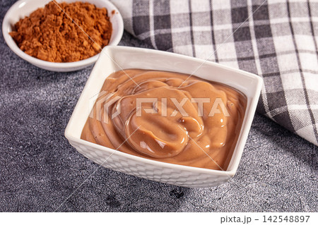 Smooth chocolate pudding in white bowl with cocoa powder and checkered cloth Smooth chocolate pudding in white bowl with cocoa powder and checkered cloth 142548897