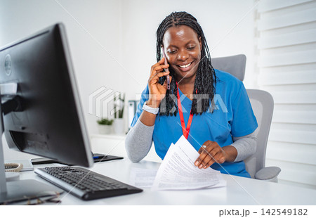 Female nurse communicating on phone while working in office Female nurse communicating on phone while working in office 142549182