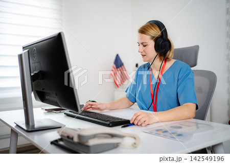 Nurse wearing headset operating computer for telehealth consultation 142549196