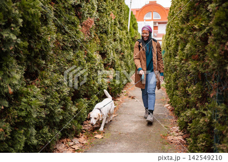 Happy young woman walking dog on street enjoying autumn Happy young woman walking dog on street enjoying autumn 142549210