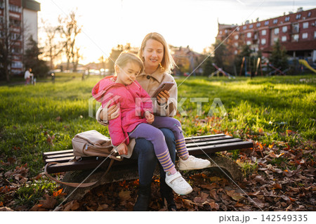 Mother and daughter using smartphone on park bench Mother and daughter using smartphone on park bench 142549335