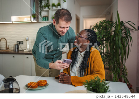 Interracial couple sharing cell phone content in kitchen 142549344