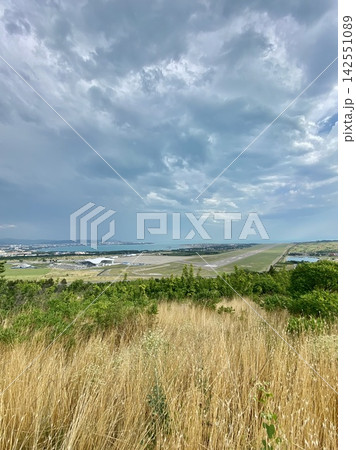Airport runway stretches toward coastline beneath dramatic storm clouds in summer landscape. Airport runway stretches toward coastline beneath dramatic storm clouds in summer landscape. 142551089