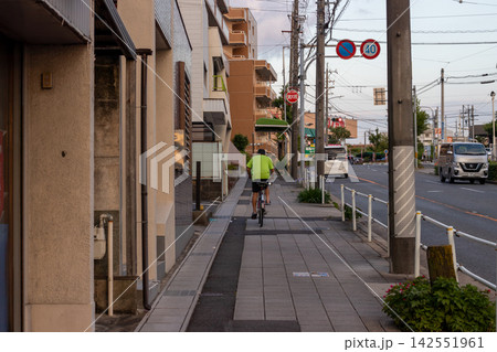 Cyclist riding along a quiet residential sidewalk Cyclist riding along a quiet residential sidewalk 142551961