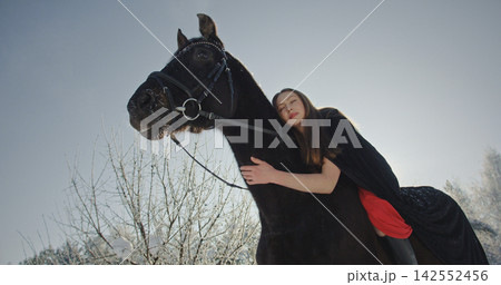 Woman embracing black horse in tranquil winter forest 142552456