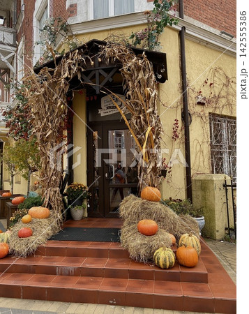 Cozy autumn cafe entrance decorated with pumpkins, hay bales and dried corn for seasonal harvest festival Cozy autumn cafe entrance decorated with pumpkins, hay bales and dried corn for seasonal harvest festival 142555386