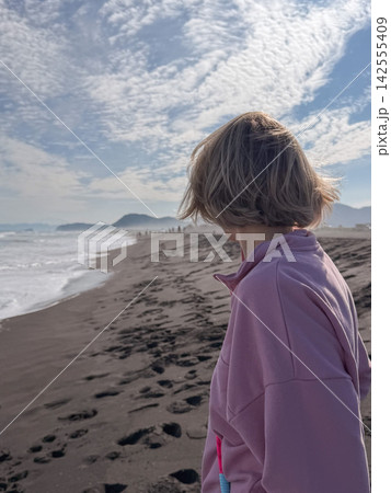 Woman looks along misty Pacific Ocean coast while standing on black volcanic sand at Khalaktyrsky Beach in Kamchatka. Contemplation, slow travel, solitude, freedom and connection with wild nature Woman looks along misty Pacific Ocean coast while standing on black volcanic sand at Khalaktyrsky Beach in Kamchatka. Contemplation, slow travel, solitude, freedom and connection with wild nature 142555409