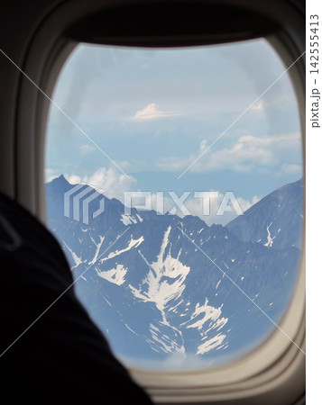 Rugged snow-covered volcanic mountains and clouds seen through airplane window during flight over Kamchatka. Air travel, remote wilderness, scenic journey, adventure and dramatic volcanic landscape 142555413
