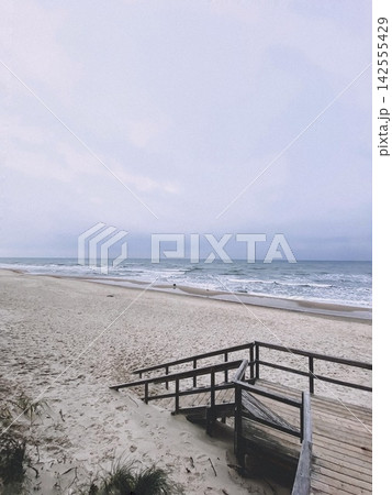 Empty sandy beach with wooden stairs leading to the sea under soft cloudy sky and calm waves 142555429
