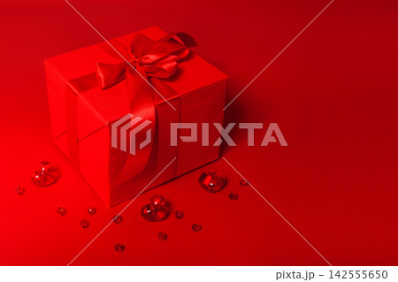 Cute red box with bow and glass shiny hearts on the red background with place for text. 142555650