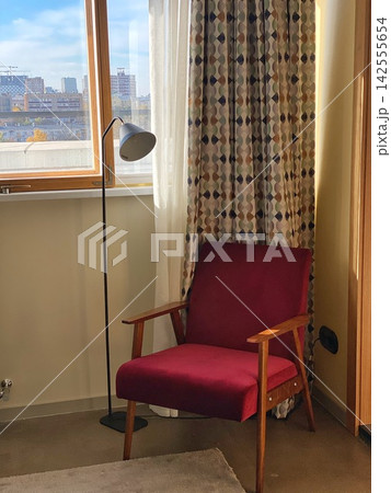 Cozy interior corner with vintage red armchair and floor lamp near window, warm sunlight creating soft shadows and home atmosphere Cozy interior corner with vintage red armchair and floor lamp near window, warm sunlight creating soft shadows and home atmosphere 142555654