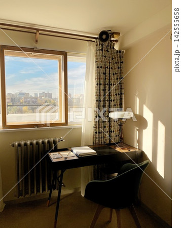 Cozy workspace by window with desk, chair and warm sunlight, minimal home office interior with city view and soft shadows Cozy workspace by window with desk, chair and warm sunlight, minimal home office interior with city view and soft shadows 142555658