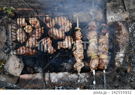 Smiling man flipping burgers on a gas grill at a backyard barbecue party. Summer outdoor cooking and social gathering concept. Man in apron grilling meat Smiling man flipping burgers on a gas grill at a backyard barbecue party. Summer outdoor cooking and social gathering concept. Man in apron grilling meat 142555932