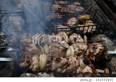 Smiling man flipping burgers on a gas grill at a backyard barbecue party. Summer outdoor cooking and social gathering concept. Man in apron grilling meat Smiling man flipping burgers on a gas grill at a backyard barbecue party. Summer outdoor cooking and social gathering concept. Man in apron grilling meat 142555935