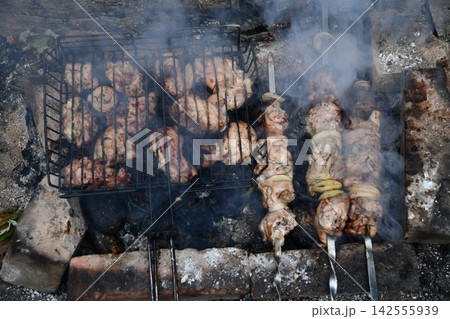 Smiling man flipping burgers on a gas grill at a backyard barbecue party. Summer outdoor cooking and social gathering concept. Man in apron grilling Smiling man flipping burgers on a gas grill at a backyard barbecue party. Summer outdoor cooking and social gathering concept. Man in apron grilling 142555939