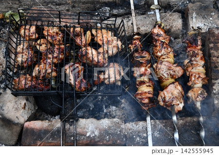Smiling man flipping burgers on a gas grill at a backyard barbecue party. Summer outdoor cooking and social gathering concept. Man in apron grilling Smiling man flipping burgers on a gas grill at a backyard barbecue party. Summer outdoor cooking and social gathering concept. Man in apron grilling 142555945