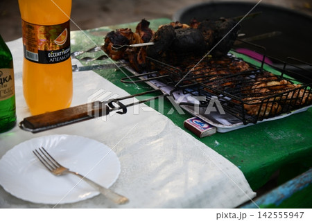 Smiling man flipping burgers on a gas grill at a backyard barbecue party. Summer outdoor cooking and social gathering concept. Man in apron grilling Smiling man flipping burgers on a gas grill at a backyard barbecue party. Summer outdoor cooking and social gathering concept. Man in apron grilling 142555947