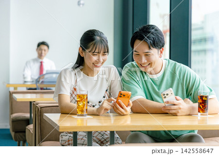 カフェでスマホを見て談笑する男女 カフェでスマホを見て談笑する男女 142558647