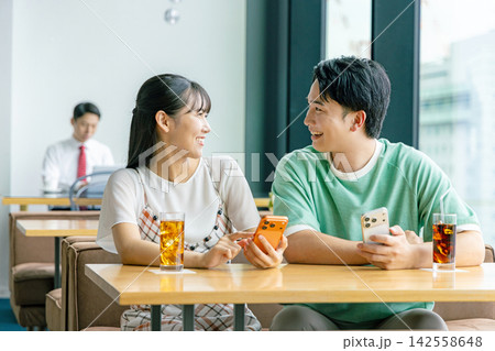 カフェでスマホを見て談笑する男女 カフェでスマホを見て談笑する男女 142558648