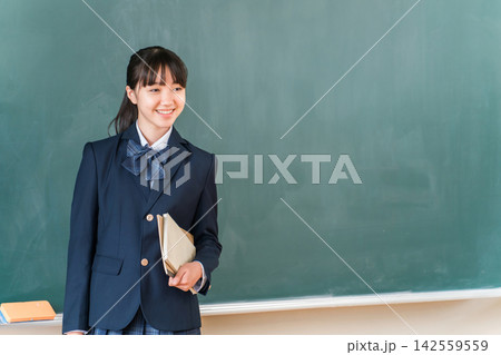 教室の黒板の前で本を持ち笑顔で発表する女子高校生。授業や学校生活、学習をイメージする教育素材 教室の黒板の前で本を持ち笑顔で発表する女子高校生。授業や学校生活、学習をイメージする教育素材 142559559