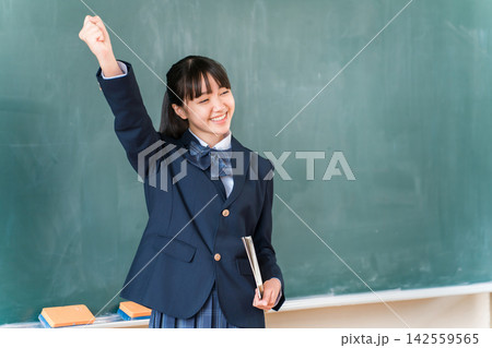 教室で大きくガッツポーズをして喜ぶ女子高校生。受験合格や目標達成、努力の成果を表す教育イメージ 142559565