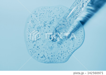 Pipette dispensing clear serum with bubbles onto light blue surface 142560971