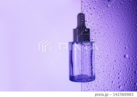 Dropper bottle behind glass background with water drops Dropper bottle behind glass background with water drops 142560983