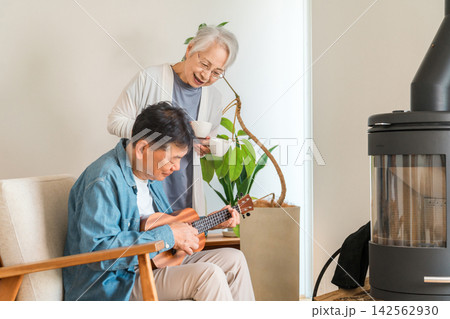 薪ストーブのある自宅でウクレレとコーヒーを楽しむ60代から70代のシニア夫婦。趣味と豊かな老後を楽し 薪ストーブのある自宅でウクレレとコーヒーを楽しむ60代から70代のシニア夫婦。趣味と豊かな老後を楽し 142562930