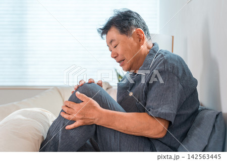 ベッドに座って膝の痛みに悩む60代から70代のシニア男性。関節痛や加齢による膝の不調のイメージ ベッドに座って膝の痛みに悩む60代から70代のシニア男性。関節痛や加齢による膝の不調のイメージ 142563445
