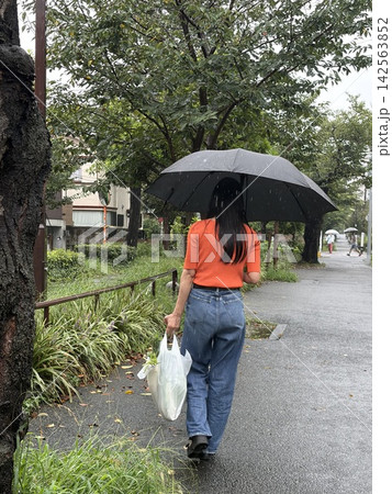 雨の日に買い物袋を持って歩く女性の後ろ姿 雨の日に買い物袋を持って歩く女性の後ろ姿 142563852