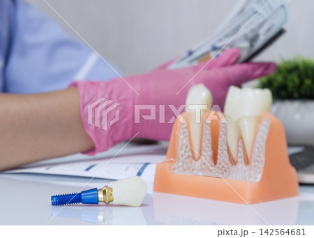 Expensive dental treatment concept showing artificial tooth implant on table and doctor holding cash dollars in background. Expensive dental treatment concept showing artificial tooth implant on table and doctor holding cash dollars in background. 142564681