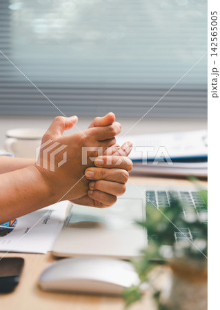 Office worker clasping hands above laptop and financial report at desk, showing a brief work break, hand stretching, stress relief, workplace wellness, ergonomics and healthy productivity routine. Office worker clasping hands above laptop and financial report at desk, showing a brief work break, hand stretching, stress relief, workplace wellness, ergonomics and healthy productivity routine. 142565005