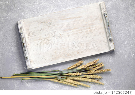 Empty white wooden tray, board with handles and dry ears of corn on gray stone table top view 142565247
