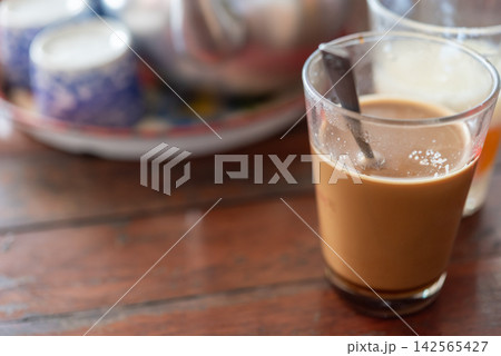 Hot milk coffee served clear glass spoon wooden table creating warm casual breakfast cafe atmosphere Hot milk coffee served clear glass spoon wooden table creating warm casual breakfast cafe atmosphere 142565427