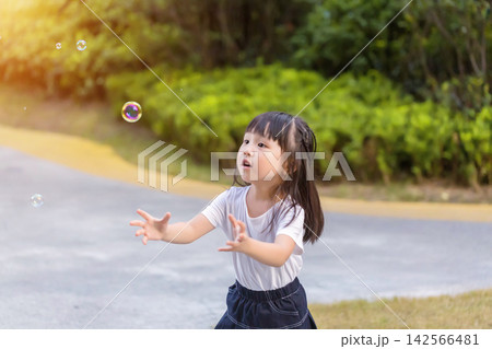 Happy Asian little girl blowing soap bubbles in sunny park, joyful childhood outdoor lifestyle Happy Asian little girl blowing soap bubbles in sunny park, joyful childhood outdoor lifestyle 142566481
