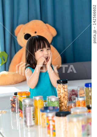 Asian little girl surrounded by snacks feeling tired, junk food overload and unhealthy diet concept Asian little girl surrounded by snacks feeling tired, junk food overload and unhealthy diet concept 142566602