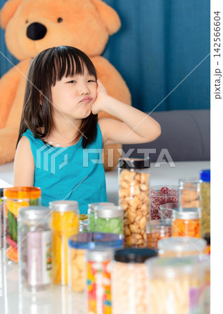 Asian little girl surrounded by snacks feeling tired, junk food overload and unhealthy diet concept Asian little girl surrounded by snacks feeling tired, junk food overload and unhealthy diet concept 142566604