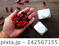Hand holding many red and black capsules 142567155