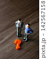 Miniature businessmen pondering a question mark, facing decision 142567158