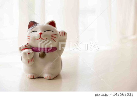 窓辺に置かれた招き猫の貯金箱 窓辺に置かれた招き猫の貯金箱 142568035