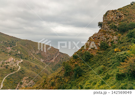 Scenic coastal mountains with winding road and distant sea under cloudy sky Scenic coastal mountains with winding road and distant sea under cloudy sky 142569049