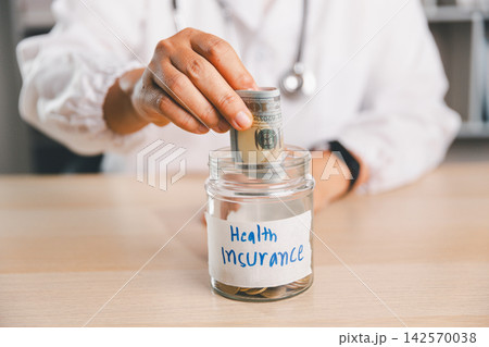 Healthcare professional counting money beside a Health Insurance savings jar, representing medical expenses, insurance costs, healthcare budgeting, financial planning and emergency savings. Healthcare professional counting money beside a Health Insurance savings jar, representing medical expenses, insurance costs, healthcare budgeting, financial planning and emergency savings. 142570038