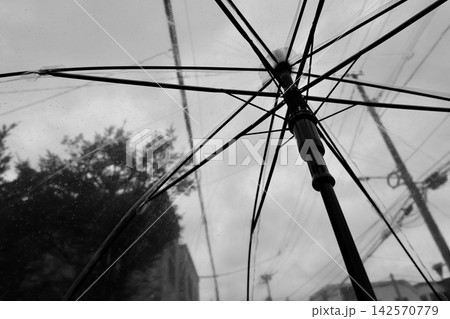 ビニール傘越しの雨が降り出した悪天候の秋空のモノクロ写真 142570779