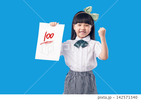 Happy Asian School Girl Holding Perfect Test Score Paper on Blue Background 142571340