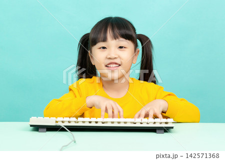 Cute Asian Little Girl Using Computer Keyboard and Smiling at Camera in Studio Background 142571368
