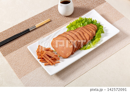 dipping sliced Chinese pine nut pork sausage into spicy chili oil, savory cold appetizer preparation dipping sliced Chinese pine nut pork sausage into spicy chili oil, savory cold appetizer preparation 142572091