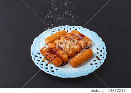 sprinkling roasted soybean powder over sweet fried glutinous rice cakes with brown sugar glaze, dark background 142572134