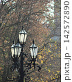 Vintage black street lamps among autumn trees with brown and yellow foliage in soft focus, creating a peaceful October park atmosphere. 142572890